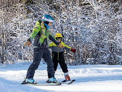 Teacher young woman and child learning alpine skiing in a school camp in Tarvisio.