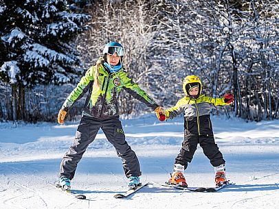 Teacher young woman and child learning alpine skiing in a school camp in Tarvisio.