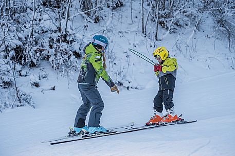 Teacher young woman and child learning alpine skiing in a school camp in Tarvisio.